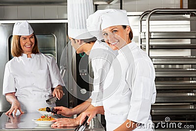 Female Chef With Colleagues In Commercial Kitchen