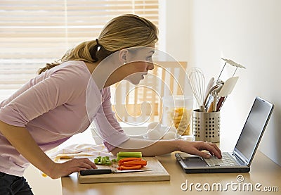 Female cooking and looking at laptop in kitchen