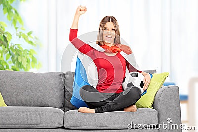 Female football fan cheering seated on sofa at home