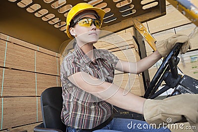 Female industrial worker driving forklift truck with stacked wooden planks in background