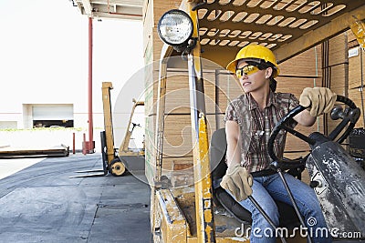 Female industrial worker looking away while driving forklift truck