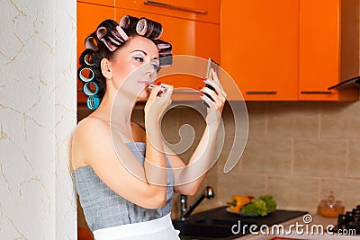 Female middle-aged housewife paints her lips in the kitchen