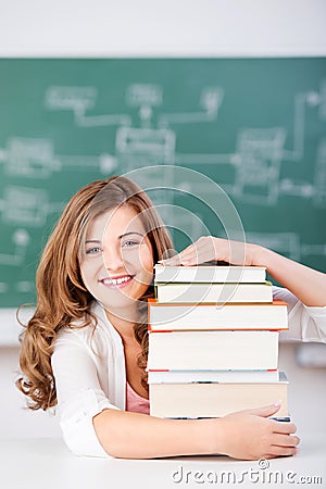 Female Student With Stack Of Books At Table In Classroom