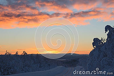 The first rays of the sun after the polar night on the road in the snow-covered Northern winter forest