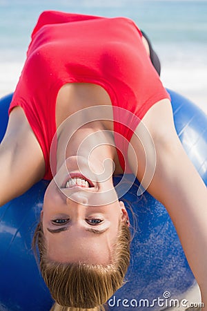 Fit blonde stretching back on exercise ball looking at camera