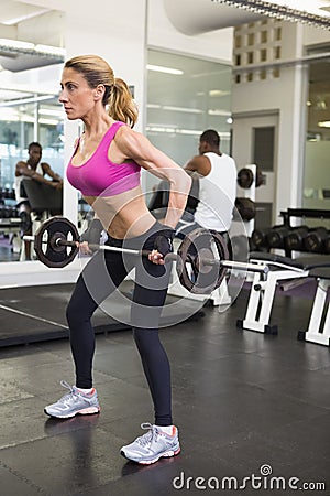 Fit young woman lifting barbell in gym