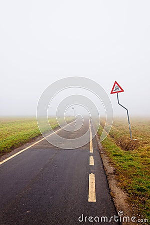 Fog along empty rural road with danger sign