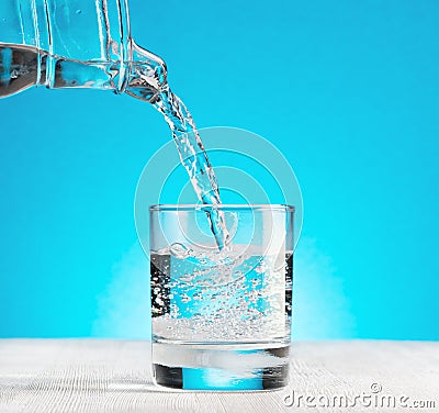 Water pouring into a glass on blue background
