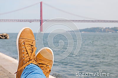 Foot an shoes. Resting near the water. Lisbon red bridge view at the background