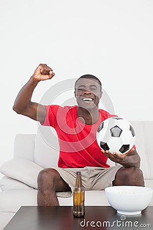 Football fan sitting on couch with ball cheering