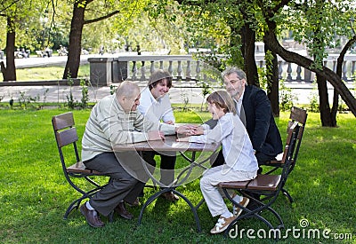 Four generations of men sitting at a wooden table in a park, laughing and talking