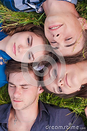 Four happy friends lying together on green grass outdoors