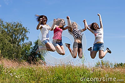 Four happy teen girls friends jumping high against blue sky