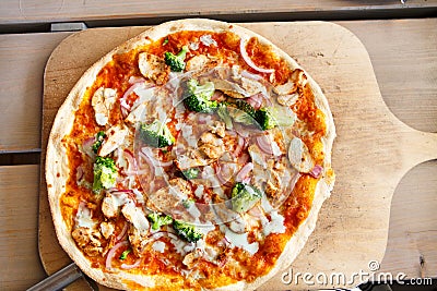 Fresh baked pizza with broccoli, chicken, onion and cheese on wo