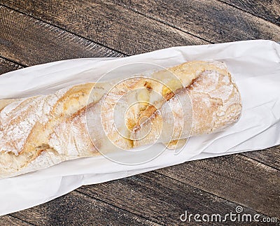 Fresh baked rustic bread loaves on paper bag on dark wood background