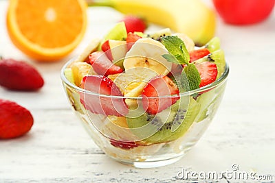 Fresh fruit salad in bowl on white wooden background.