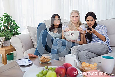 Friends sharing bowl of popcorn and watching television