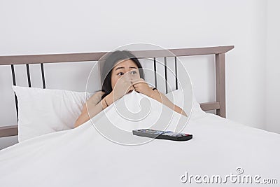 Frightened woman watching TV in bed