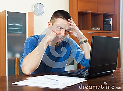 Frustrated man studying financial information on laptop