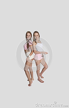 Full length of female friends wearing hot pants posing over gray background