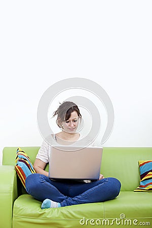 Full length of happy young woman using laptop while sitting on green sofa