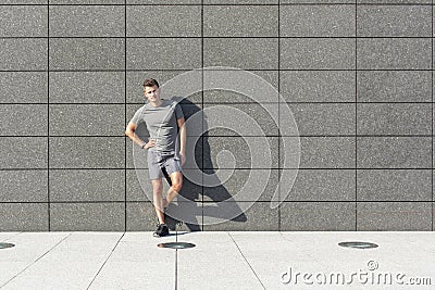 Full length portrait of confident sporty man leaning on tiled wall