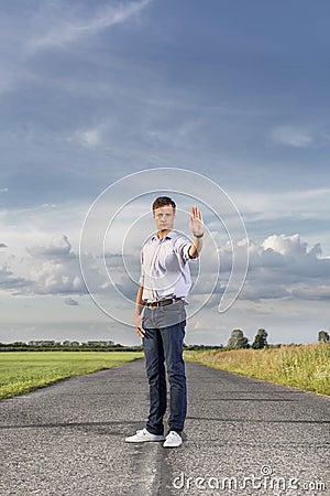 Full length of serious young man holding up hand to stop at country road