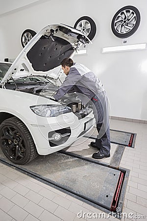 Full length side view of male automobile mechanic repairing car engine in repair shop