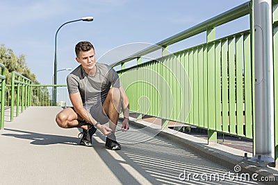 Full length of sporty man tying shoelace on bridge