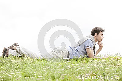 Full length of thoughtful young man lying on grass against clear sky