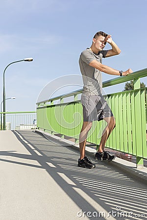 Full length of tired man wiping sweat on bridge after jogging