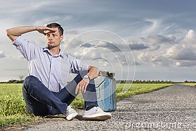 Full length of young man shielding eyes while sitting with petrol can by country road