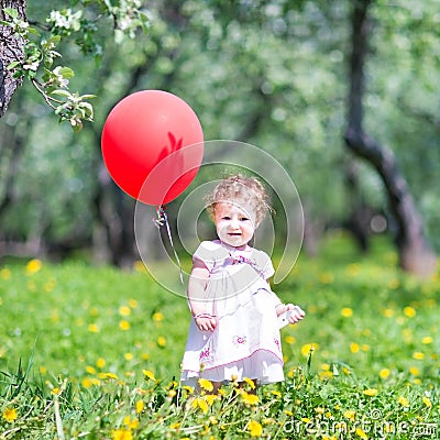 Funny baby girl with a red balloon in a garden