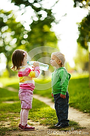Funny boy and girl drinking mineral water in park