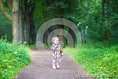 Funny curly baby girl in rain boots walking in a park