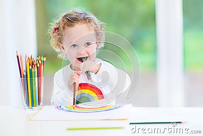 Funny laughing baby girl drawing at a white desk