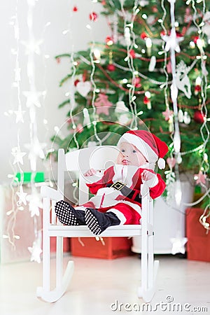 Funny newborn baby boy in Santa costume sitting under Christmas tree