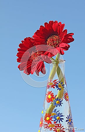 Gerber daisies in a hand painted glass vase, blue sky