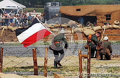 German soldier runs with by a German flag.