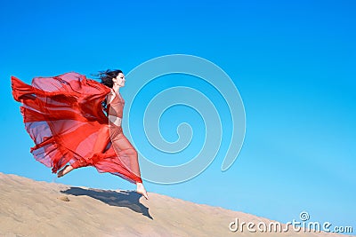 Girl in airy red dress running on sand dunes