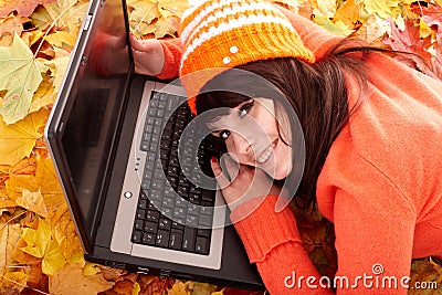 Girl in autumn orange leaves with laptop