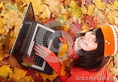 Girl in autumn orange leaves with laptop.