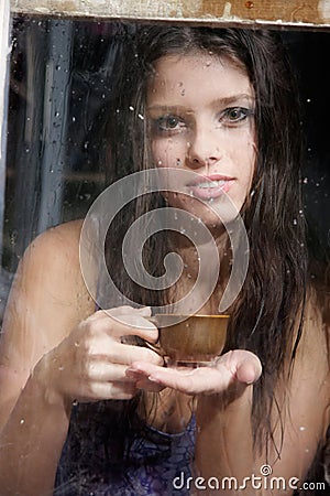 Girl with cup of tea behind wet window