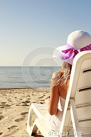 Girl in hat is lying on a deck chair on the beach