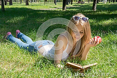Girl holding a red apple and reading a book in a summer