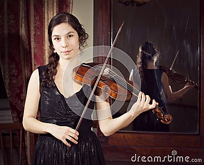 Girl playing vintage violin near huge vintage mirror