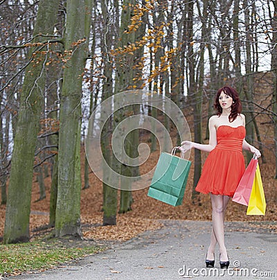 Girl in red dress with shopping bags walking in park