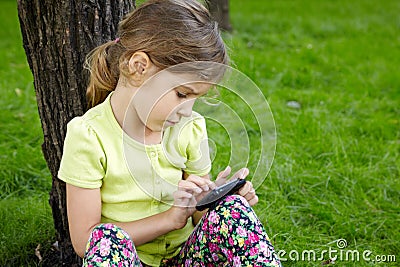 Girl sits in park and plays with cell phone