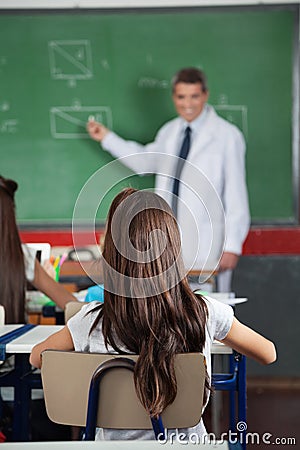 Girl Sitting At Desk With Teacher Teaching In