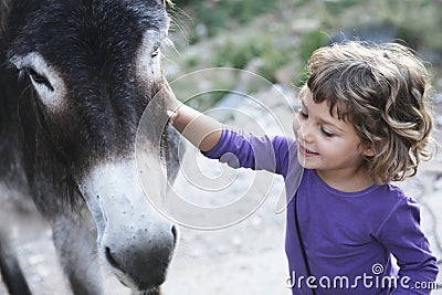 Girl smiling petting to donkey